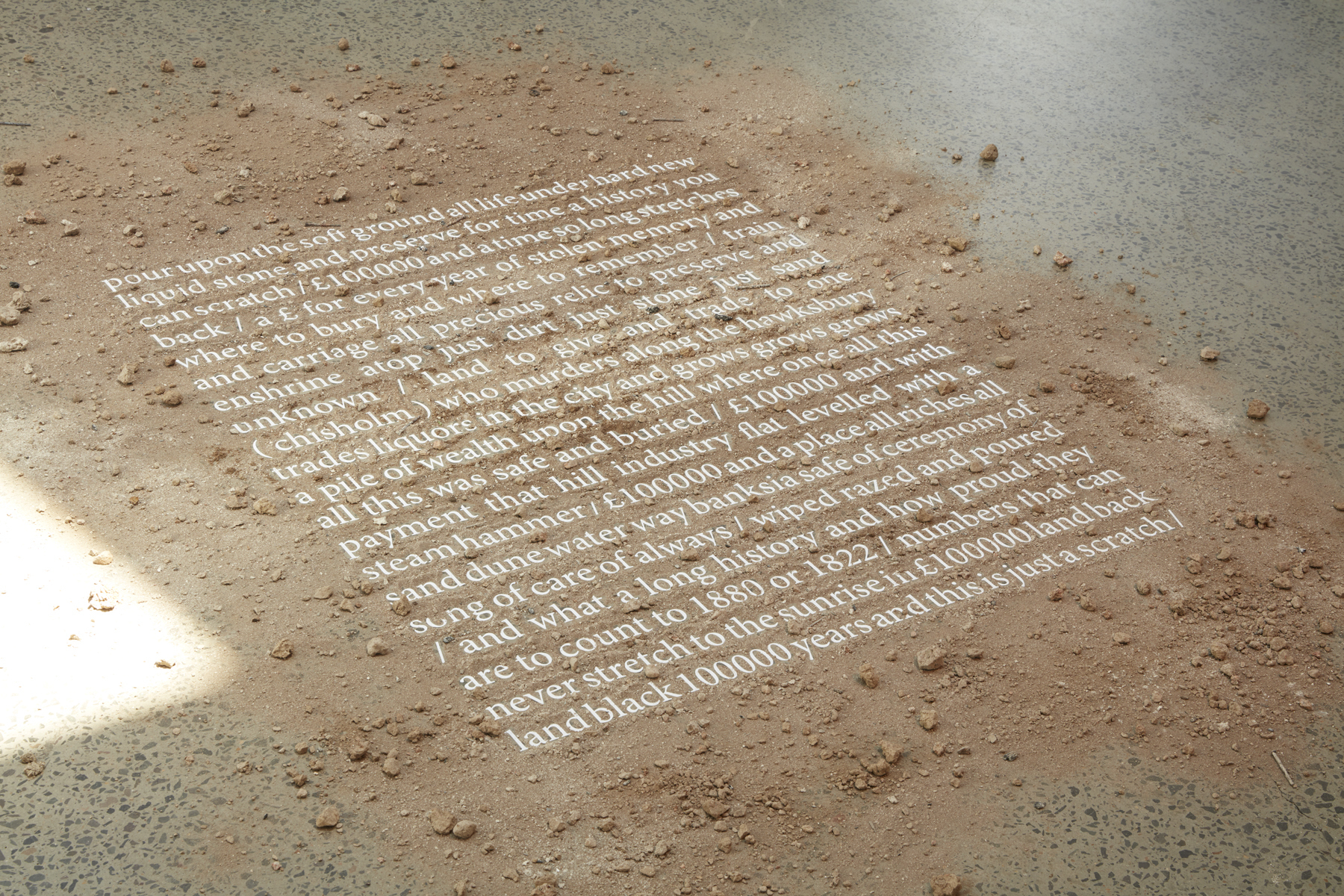 White text of a poem can be read through a thin layer of dirt.